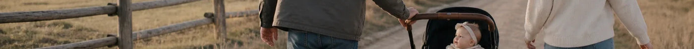 Forældre går tur med deres lille pige i en sort barnevogn ad en stille sti på en ranch efter solopgang.