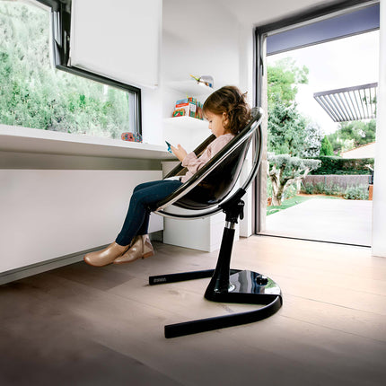 Young girl seated in a mima moon Black Chair in junior chair mode by a window