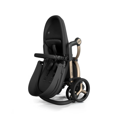 mima xari max full-size stroller folded upright on its rear wheels, Champagne chassis and matching spokes