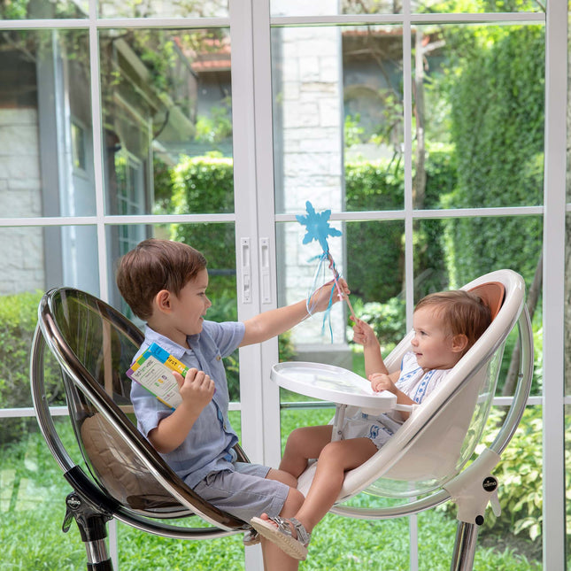Boy in a mima moon Black Chair playing with a toddler in a White Chair in high chair mode
