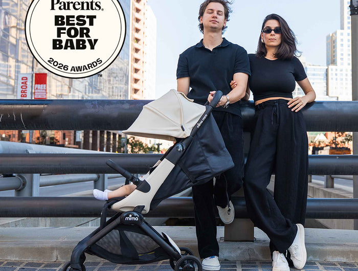 Parents beside a mima miro Black compact travel stroller in the city with a 2026 award badge
