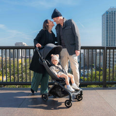 Parents on a rooftop city overlook with a toddler riding in the mima miro Black travel stroller