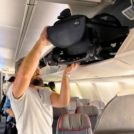 A parent lifting the folded mima miro Black travel stroller into an airplane overhead bin