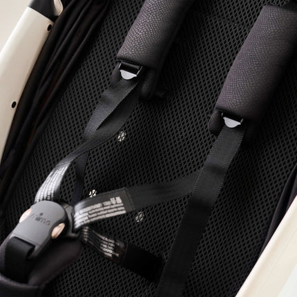 Close-up of the padded shoulder straps and magnetic buckle over the black mesh summer pad in the mima miro White stroller