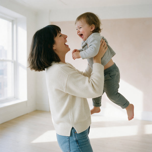A mother lifts her laughing toddler in a bright room