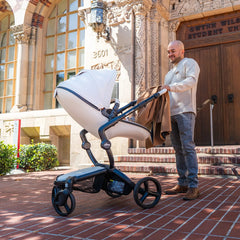 A parent pushing the mima xari max White stroller with a coat draped over the handlebar